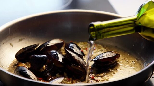 Cooking delicious fresh mussels on hot pan in luxury restaurant. Pouring dish with white dry wine. Traditional mediterranean cuisine. Slow motion scene.