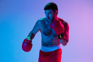 One man, professional boxer in sportwear boxing on studio background in gradient neon light. Concept of sport, activity, movement, wellbeing.