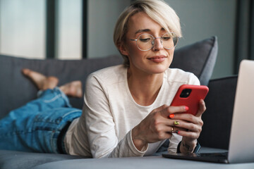 Smiling mid aged blonde woman using mobile phone - obrazy, fototapety, plakaty