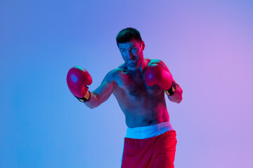 Portrait of Caucasian man, professional boxer in sportwear boxing on studio background in gradient...