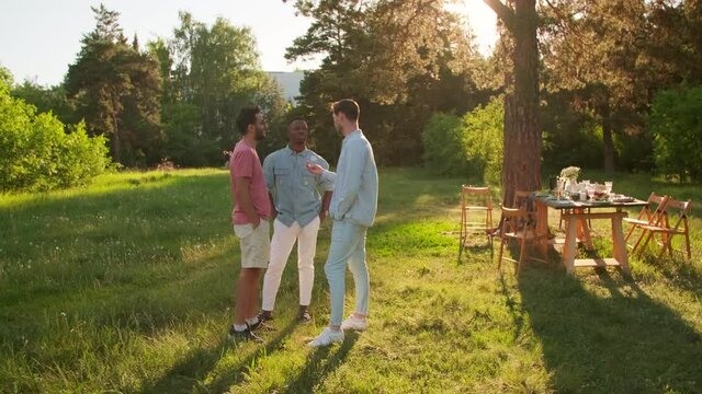 Horizontal long shot footage of three young multi-ethnic men spending time together in park chatting about something