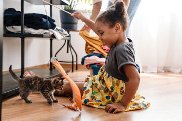 Black girl smiling and playing with kitten while sitting on floor
