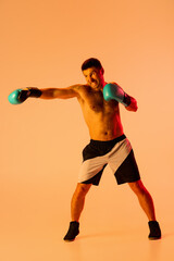 Fototapeta na wymiar Portrait of Caucasian man, professional boxer in sportwear boxing on studio background in yellow neon light. Concept of sport, activity, movement, wellbeing.