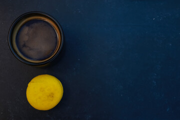 Black coffee cup and yellow macaroon top view. Dark mug of espresso or Americano, lemon sweet biscuit on concrete table background. For coffee shop templates, cafe, morning, dessert concept