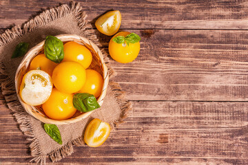 Ripe yellow tomatoes with fresh basil in a wicker basket
