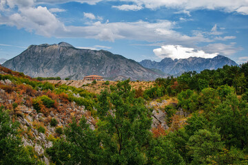 View of canyon in Albanian mountains. Summer landscape with green trees, house on rocky hills and blue sky.