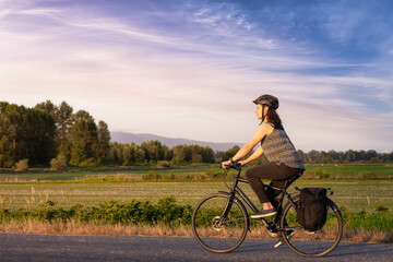 Adventurous White Cacasusian Woman riding a bicycle on a road. Sunny Summer Sunset Art Render. Barnston Island, Vancouver, British Columbia, Canada. Adventure Journey Concept