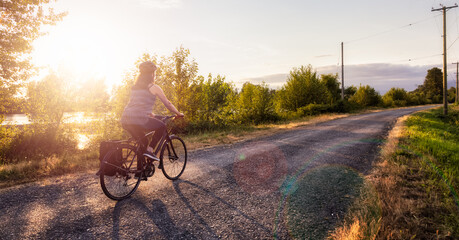 Adventurous White Cacasusian Woman riding a bicycle on a road. Sunny Summer Sunset. Barnston...