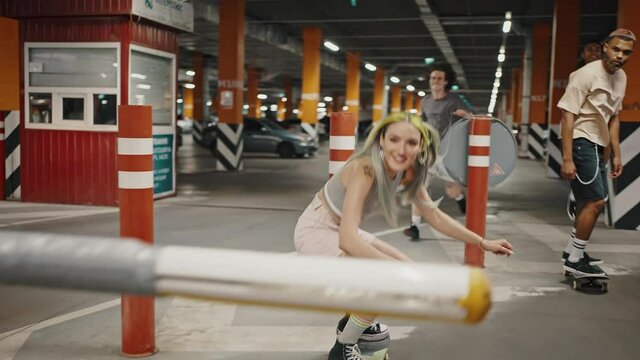 Company of happy young diverse friends having fun at underground parking, riding skateboards and jumping together