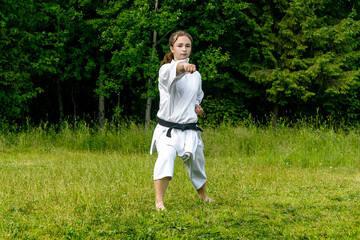 teenage girl training karate kata outdoors, performs punch seiken chudan tsuki