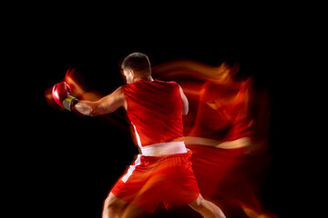 Back view. One professional boxer in red shorts and gloves training, exercising over black...