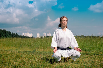 teenage girl karateka before starting training outdoor enters the mokuso meditative state in the seiza pose