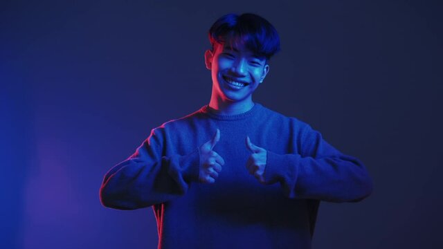 Like gesture. Neon light people. Approval sign. Perfect choice. Red blue color supportive satisfied pleased smiling Asian guy showing thumbs up isolated on dark night.