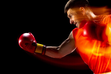 Punch, uppercut. Cropped portrait of professional male boxer training on black studio background in...