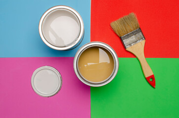 Cans of paint and a brush stand on a colored background. Renovation in the room