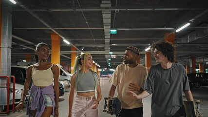 Group of positive diverse friends walking together at underground parking, laughing together, guy giving high five