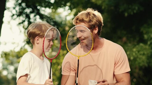 A father is teaching his son playing badminton in the park at summer