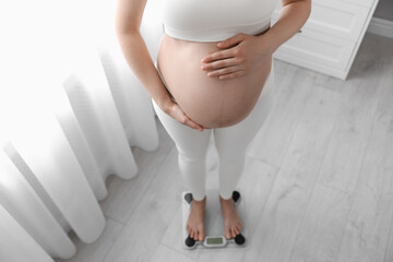 Pregnant woman standing on scales at home, closeup