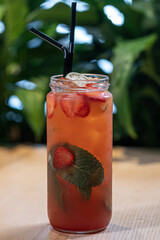 strawberry lemonade drink with mint in glass bottle and ice near green plant