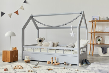 Stylish scandinavian child's room with creative wooden bed, wooden cube, lamp, wooden shelf, plush and wooden toys and hanging textile decorations. Grey walls, carpet on the floor. Template.