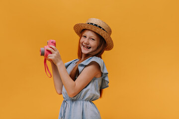 Happy excited redhead girl in dress and boater smiles sincerely. Cool cheerful child in denim...