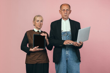 Serious elderly man and woman in retro vintage farmer outfits isolated on pink studio background. Retro style, comparison of eras and cultural concept.