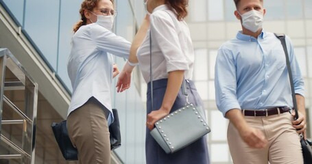 Low angle view of colleagues in safety mask greeting with elbow bump in front of office building