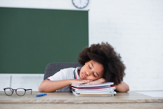 African american schoolchild sleeping on notebooks near eyeglasses in classroom