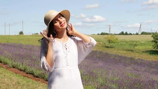 Close up of beautiful smiling woman in hat near lavender field. Summer time. Selective focus of girl with long hair enjoying sunny day scent of aromatic flowers . Copy space