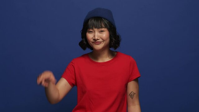 A smiling asian woman is doing looser gesture standing isolated over blue wall in the studio