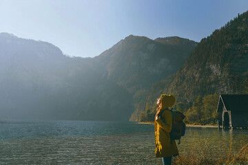 side view of a girl in a yellow autumn jacket with a backpack in the mountains looks at the sun on the background of the lake