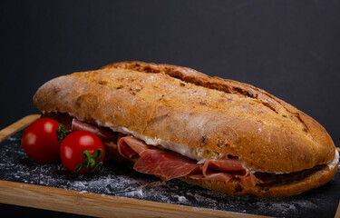 Ciabatta sandwich with cream cheese and prosciutto on a wooden tray