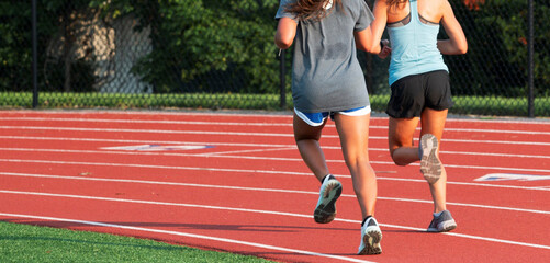 Two girls running on the curve of a red track