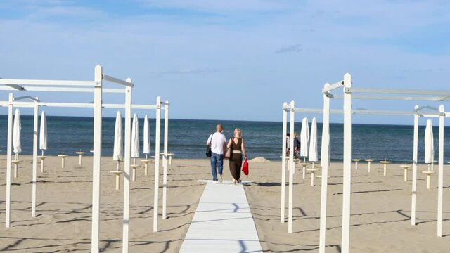 Slow motion shooting of a couple walking towards the sea in a beautiful beach in the Riviera Romagnola area of Riccione, in an off season spring day.