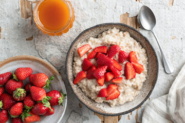 Oatmeal porridge bowl with strawberries and honey on concrete background, table top view. Clean eating, dieting concept