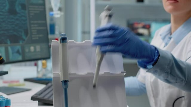 Close up of scientific micropipette on laboratory desk used by biotechnology specialist in lab coat while typing on computer. Woman working in medical development and innovation industry