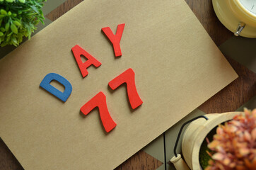Day 77, cover design in natural concept with the alphabet on brown notebook on the wooden table for a background.