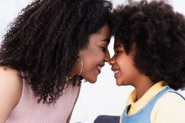 Side view of african american mother and daughter standing nose to nose at home
