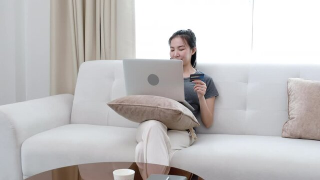 Asian woman sitting on sofa, Using laptop to shop online with credit card to register for payment ,Online transactions.