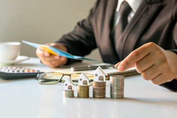 Businessman putting coins on a pile of coins with financial concept house model. Mortgage and Real Estate Mortgage