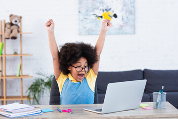Excited african american kid looking at laptop while doing schoolwork