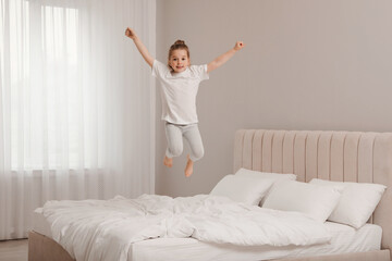 Fototapeta na wymiar Cute little girl jumping on bed at home