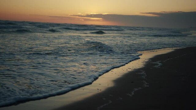 4k closeup footage of sea waves wahing off footprints on the golden sand at beach