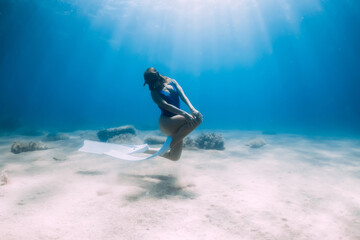 Female free diver with fins posing underwater in blue sea with sunlight.