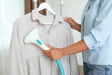 Woman steaming blouse on hanger at home, closeup