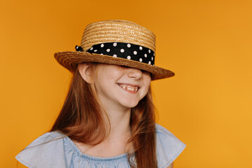 Good-humored optimistic redhead little girl in boater and blue blouse smiles sincerely. Happy...