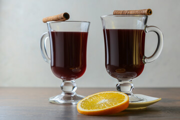 Mulled wine in glass cups with cinnamon and oranges on a wooden table.