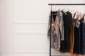 Collection of trendy women's garments on rack near white wall indoors, space for text. Clothing...