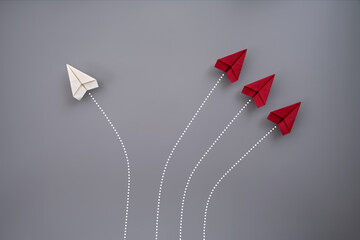 One white and three red folded paper planes flying against gray background