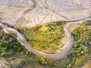 At the foot of mountainous white sediments, a winding mountain river flows, autumn trees. Sayan Mountains in Tuva